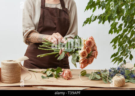 Female florist making beautiful bouquet from living coral color roses on a light background. Process step by step Stock Photo