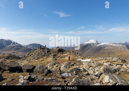 Walkers on the Western Top of Glaramara with the Snow Capped Mountains (L to R) of Great End, Lingmell, Great Gable, Green Gable and Pillar, Lake Dist Stock Photo