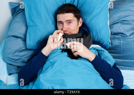 Photo of sick man using nasal spray while lying in bed Stock Photo