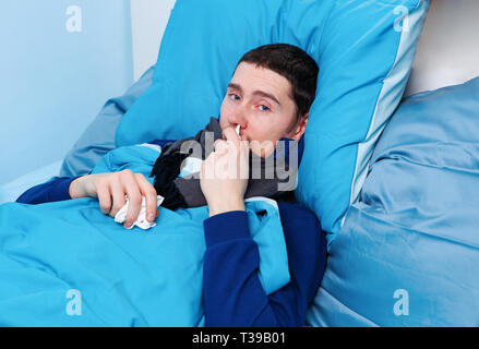 Image of sick brunet man using nasal spray while lying in bed Stock Photo