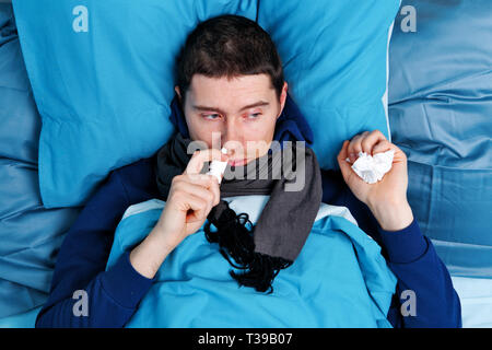 Sick brunet man using nasal spray while lying in bed Stock Photo