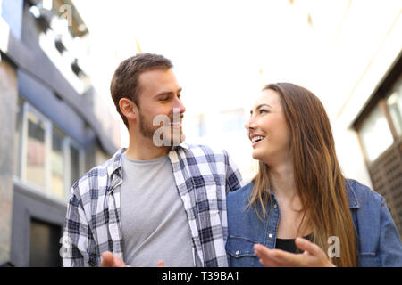 Front view of a happy couple walking in the street talking looking each other Stock Photo