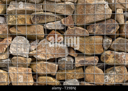 A close up of a pile of granite rocks in a metal cage used for flood prevention, mostly brown in colour behind metal Stock Photo