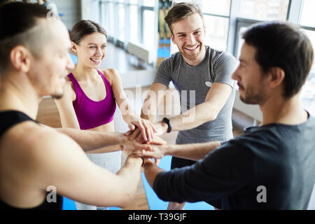Smile man and women making hands together in fitness gym. Group of young  people doing high five gesture in gym after workout. Happy successful  workout class after training. Teamwork concept Stock Photo
