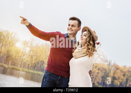 Honey, look over there. Low-angle view of handsome man embracing his beautiful girlfriend and pointing away while standing outdoors. Young couple in l Stock Photo