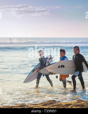 PENICHE, PORTUGAL - OCTOBER 20, 2018: Three boys in wetsuits with surfboards at ocean coast, Peniche, Portugal Stock Photo
