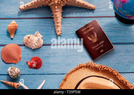 From above summer straw hat near world globe, sea stars with seashells, and Thai passport book on blue wooden background Stock Photo