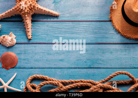 From above summer hat near rope and sea stars with seashells on blue wooden background Stock Photo