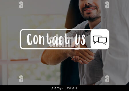 Businessmen shaking hands together in office in background - with Contact Us message Stock Photo