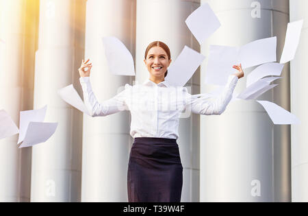 Celebrating success. Portrait of young and beautiful business woman in skirt and shirt throwing up papers and smiling while standing against white pil Stock Photo