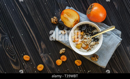 Oatmeal with Persimmon, Prune, Dried Apricots, Walnut and Sesame on a Black Wooden Table Top View Copy Space Background Stock Photo