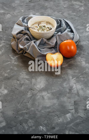 Oatmeal with Persimmon and Pumpkin Seeds on a Gray Rough Decorative Surface Top View. Copy Space Stock Photo