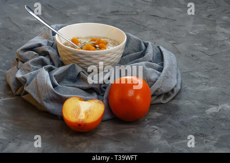 Oatmeal with Persimmon and Pumpkin Seeds on a Gray Rough Decorative Surface Top View. Copy Space Stock Photo
