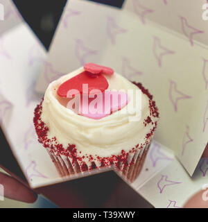 A red velvet cupcake decorated with sugar hearths in a box. Square format. Stock Photo