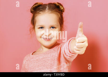 Closeup portrait of a cute attractive little child girl showing thumb up over pink background. Stock Photo