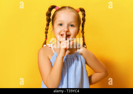 Closeup portrait of cute attractive little child girl showing shh sign over yellow background. Stock Photo