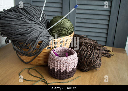 Traditional colorful yarns for hobby knitting in a straw eco basket on a light wooden surface, knitting needles, knitted basket. Stock Photo