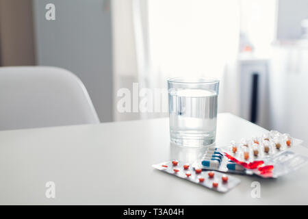 Different pills and glass of water on kitchen table. Healthcare and medicine concept Stock Photo