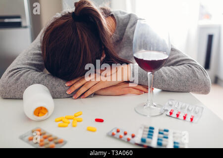 Woman took lots of pills with wine on kitchen. Suicide and depression concept. Mental disorder Stock Photo