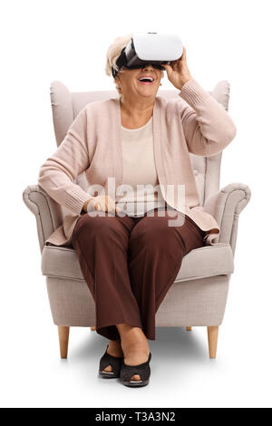 Excited elderly woman sitting in an armchair and using a VR headseat isolated on white background Stock Photo