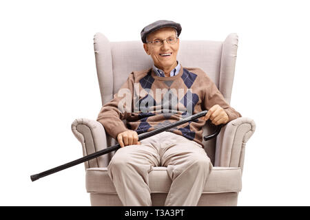 Elderly man with a walking cane sitting in an armchair and smiling at the camera isolated on white background Stock Photo