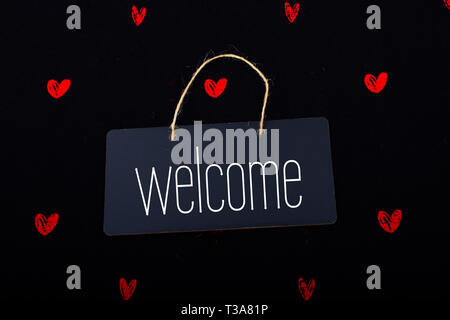 Welcome wording on black notice board  with red hearts around Stock Photo