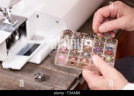 Close up on seamstress hands choosing threads for electrical sewing machine . Stock Photo