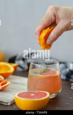 Ripe grapefruit and oranges with grapefruit juice on wooden table.Woman is squeezing a slice of orange into glass Stock Photo