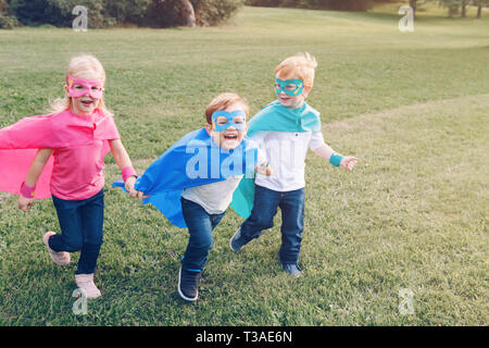 Cute adorable preschool Caucasian children playing superheroes. Three kids friends having fun together and running outdoors in park. Happy active chil Stock Photo