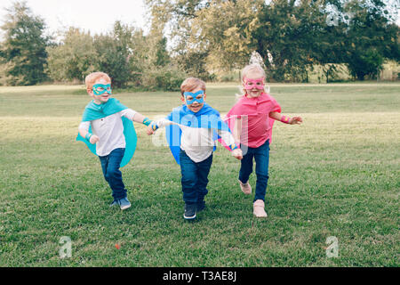 Cute adorable preschool Caucasian children playing superheroes. Three kids friends having fun together and running outdoors in park. Happy active chil Stock Photo