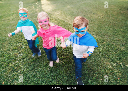 Cute adorable preschool Caucasian children playing superheroes. Three kids friends having fun together and running outdoors in park. Happy active chil Stock Photo