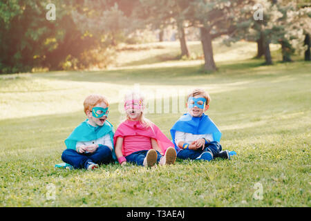 Cute preschool Caucasian children playing superheroes. Three kids friends having fun together outdoors in park. Happy active childhood and friendship  Stock Photo