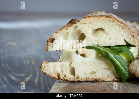 Close up Brie sanwdich in French baguette, made of Brie de Meaux Cheese with slices of rucola rocket salad and walnuts on a rustic wooden table. This  Stock Photo