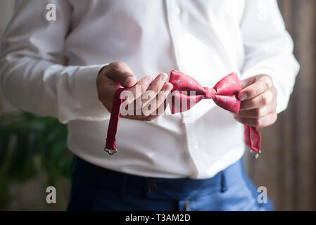 Red bow tie in the hands of a man in a white shirt close-up Stock Photo