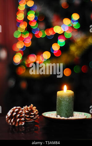Christmas still life with pine cones and a green candle on a background of colored lights Stock Photo