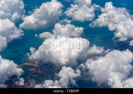 Beautiful view from window of plane flying over white clouds, sea surface and island. Natural panorama with clouds. White clouds moving above water su Stock Photo