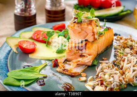 A piece of baked red fish with a side dish of sprouts and avocado salad. Macrobiotic food concept. Healthy food. Stock Photo