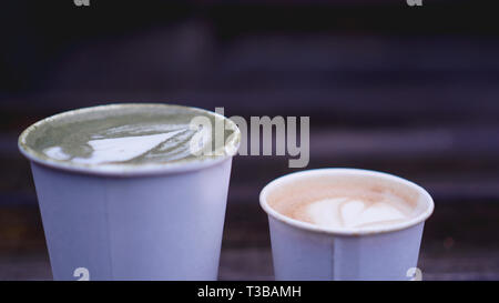 Cup of matcha tea with latte art and cappuccino in paper cup on wooden background. Blurred background. Stock Photo