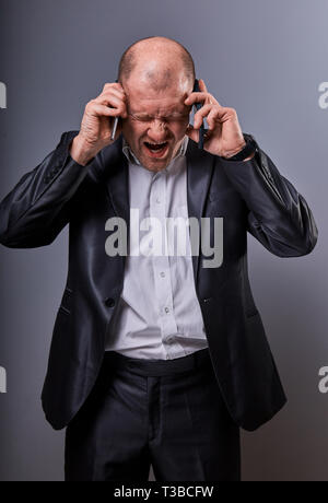 Unhappy loud crying angry business man talking on mobile phone very emotional wide opened mouth in office suit on grey background. Closeup portrait Stock Photo
