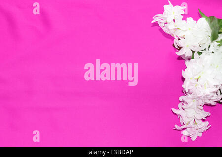 The texture of silk fabric. The material is pink-red. Close-up. There is a white flower on the texture. Stock Photo