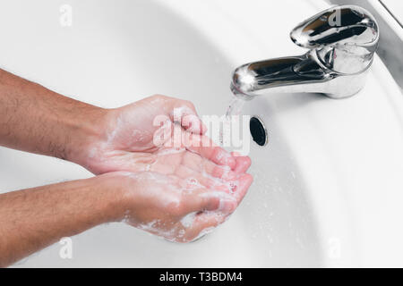 Adult caucasian male washing hands with soap under the faucet with water