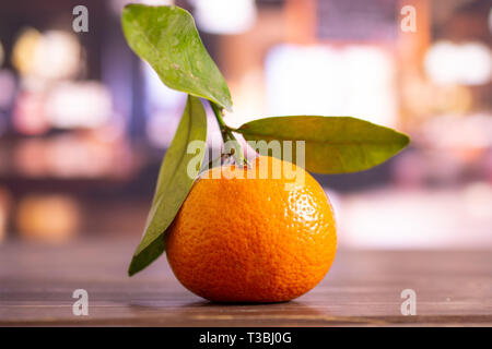 One whole fresh orange mandarine with green leaves in a restaurant Stock Photo