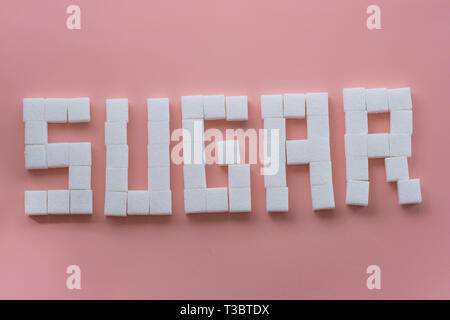 Sugar cubes used to spell the word sugar on a pink background Stock Photo