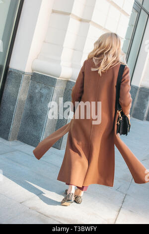 Stylish fashionable woman wearing beige coat with curly blonde hair from back at the street Stock Photo