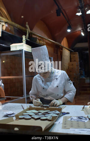 Lviv, Ukraine. 13 March 2016. Person working inside of the Lviv Homemade Chocolate Factory. Store view through the shop window, woman producing chocol Stock Photo