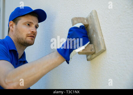 worker applying decorative facade plaster on house wall Stock Photo