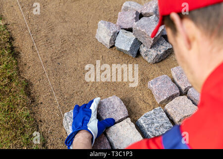 pavement construction - worker laying granite stone pavers Stock Photo