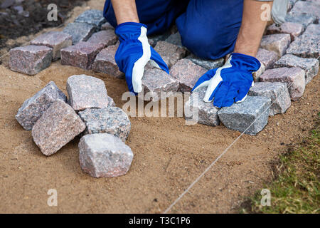 garden path construction - worker laying granite stone pavers Stock Photo