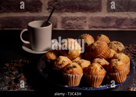 group of muffins with chocolate on a blue plate next to a cup of milk Stock Photo