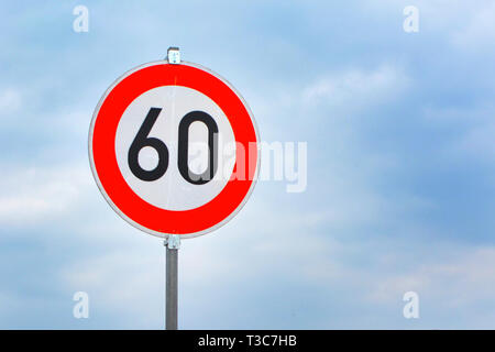 A round roadsign with the number 60 on it against a blue cloudy sky ...